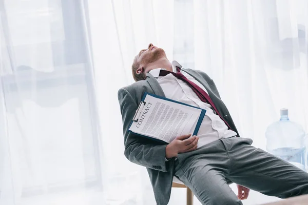 Exhausted businessman sleeping on chair with contract in hand at office — Stock Photo