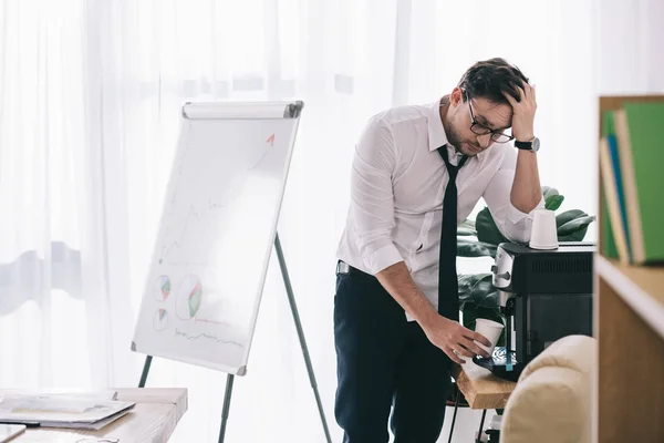 Young overworked businessman pouring coffee from office machine — Stock Photo