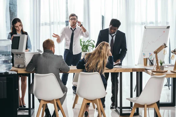 Grupo de empresarios conversando en la oficina mientras el jefe habla por teléfono - foto de stock