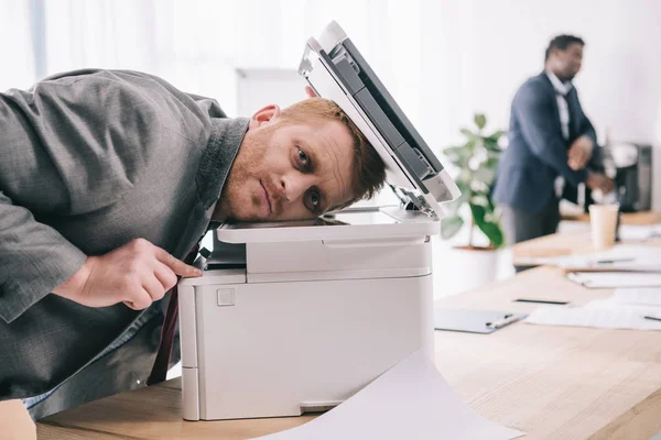 Giovane uomo d'affari oberato di lavoro appoggiato alla fotocopiatrice in ufficio — Foto stock