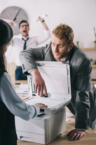 Uomo d'affari aiutare collega con fotocopiatrice in ufficio — Foto stock