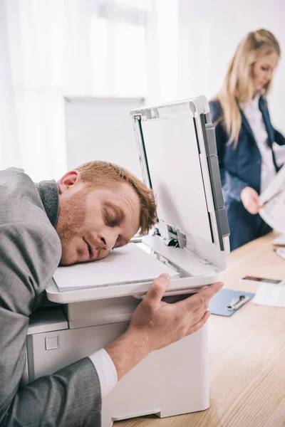 Jovem empresário sobrecarregado dormindo com a cabeça na copiadora no escritório — Fotografia de Stock