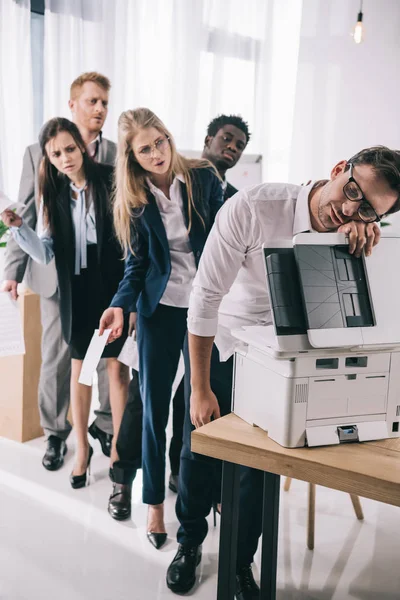 Uomo d'affari che dorme sulla fotocopiatrice mentre i suoi colleghi in coda dietro di lui — Foto stock