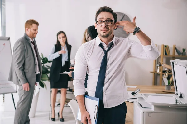 Exhausted young manager making handgun gesture at office and looking at camera — Stock Photo