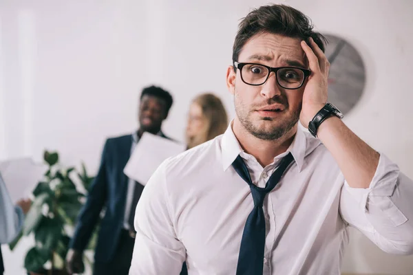 Bewildered young businessman touching head and looking at camera at office — Stock Photo