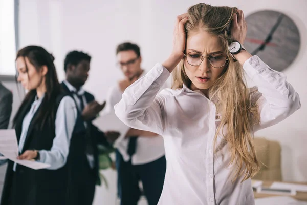 Bewildered young businesswoman holding head in hands at office — Stock Photo