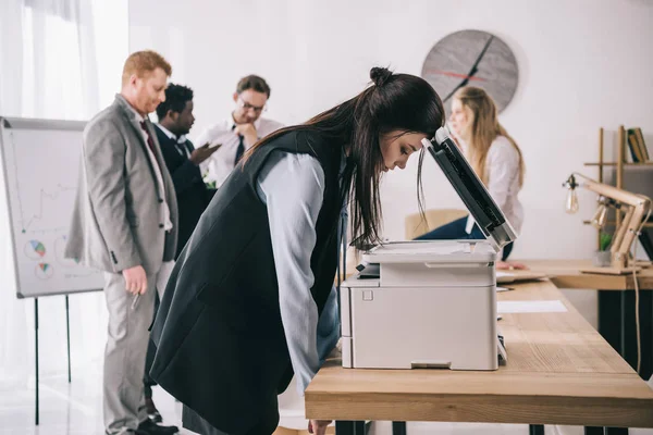 Exhausted sleepy businesswoman leaning on copier at office while colleagues having conversation — Stock Photo