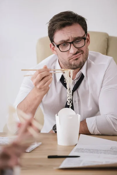 Jeune homme d'affaires dégoûté avec une boîte de nouilles à emporter sur le lieu de travail — Photo de stock