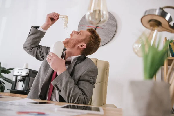 Overworked young businessman eating take away noodles at workplace — Stock Photo