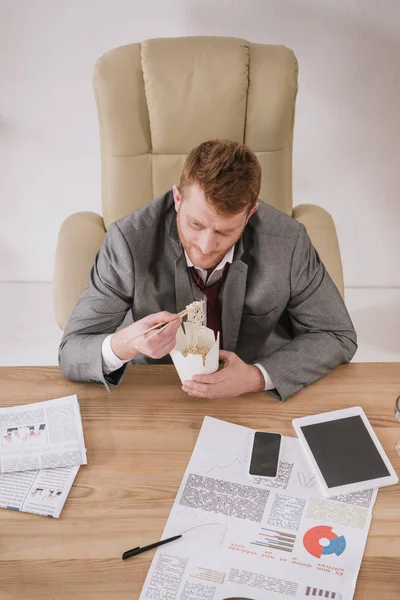 High angle view of overworked young businessman with box of take away noodles at workplace — Stock Photo