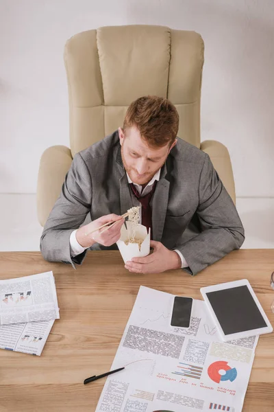 Vue grand angle de jeune homme d'affaires surmené avec boîte de nouilles à emporter sur le lieu de travail — Photo de stock