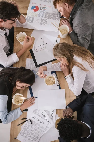 Blick von oben auf ein überarbeitetes Businessteam, das mit Schachteln Nudeln am Konferenztisch schläft — Stockfoto