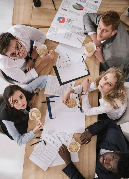 Vista superior da equipe de negócios sobrecarregada comer macarrão na mesa de conferência — Fotografia de Stock