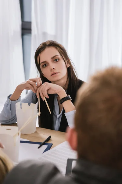 Jeune gestionnaire surmené assis sur le lieu de travail avec boîte de nourriture chinoise et baguettes — Photo de stock