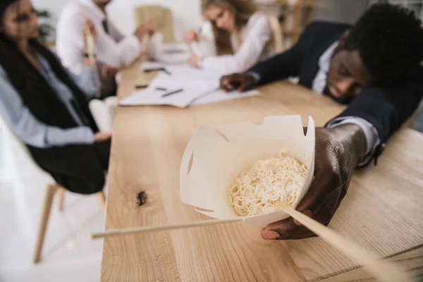 Primer plano de hombre de negocios durmiendo en la sala de conferencias con caja de fideos en la mano - foto de stock