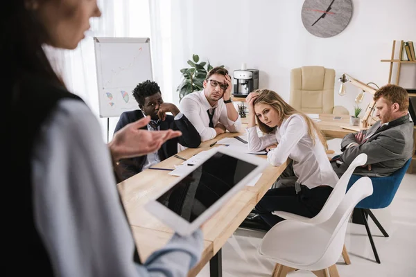 Overworked businesspeople sitting at conference hall and listening to colleague with tablet at office — Stock Photo