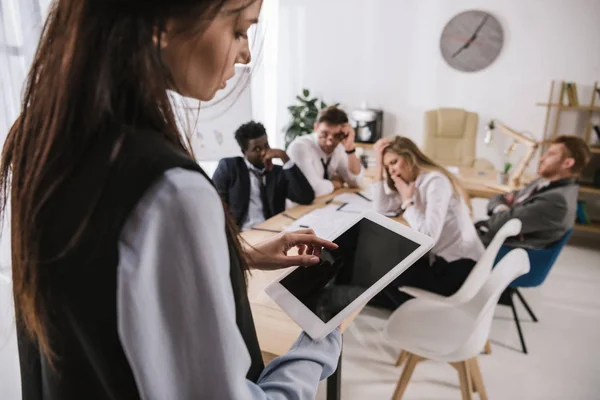 Femme d'affaires utilisant une tablette numérique avec des collègues flous assis dans la salle de conférence sur fond — Photo de stock