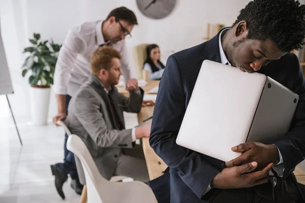 Tired businessman sleeping while holding laptop in hands at office — Stock Photo