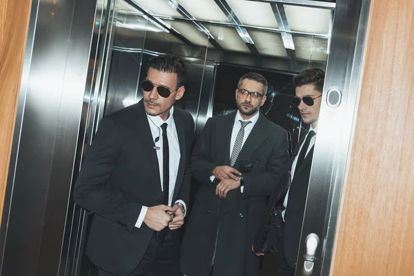 Bodyguards looking out from elevator and businessman looking at watch — Stock Photo