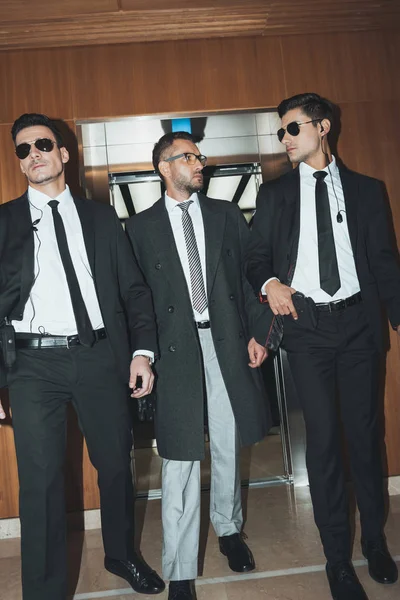 Bodyguards and businessman walking from elevator in business center — Stock Photo