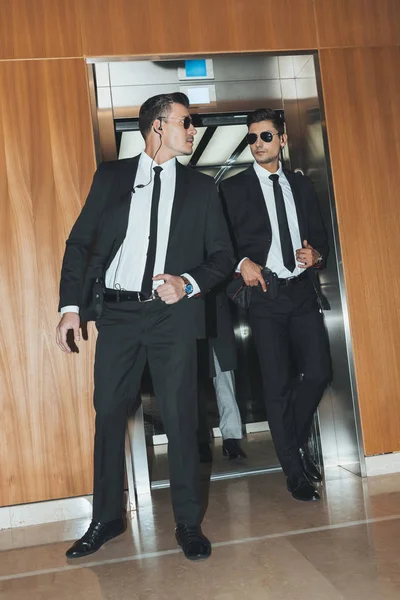 Bodyguards reviewing territory when going out from elevator with businessman — Stock Photo