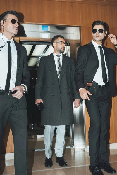 Businessman going out from elevator with two bodyguards — Stock Photo