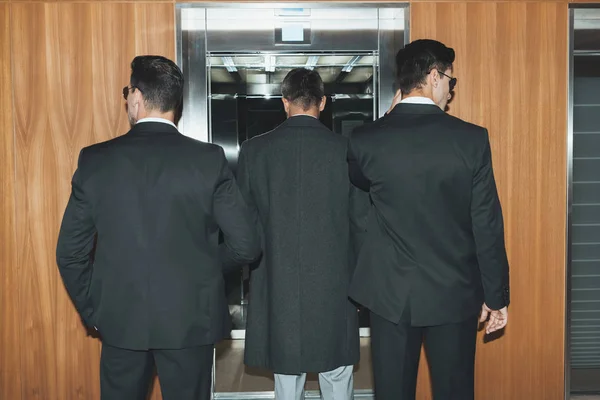 Back view of bodyguards and businessman standing at elevator — Stock Photo
