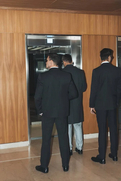 Rear view of bodyguards and politician standing at elevator — Stock Photo