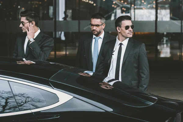 Bodyguards going with businessman and reviewing territory near car — Stock Photo