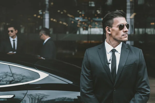 Bodyguard standing at businessman car and reviewing territory — Stock Photo