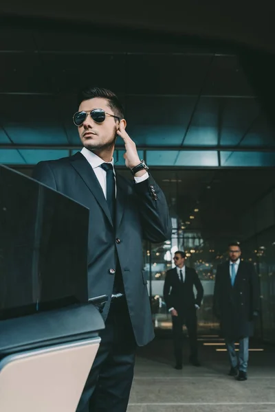 Bodyguard opening car door for businessman and listening security earpiece — Stock Photo