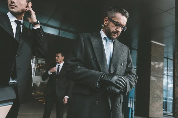 Businessman looking at watch and standing with bodyguards — Stock Photo