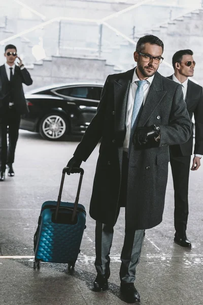 Hombre de negocios guapo caminando con bolsa de viaje desde el coche y mirando el reloj - foto de stock