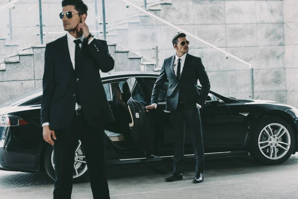 Bodyguards in sunglasses standing at car and waiting for politician — Stock Photo