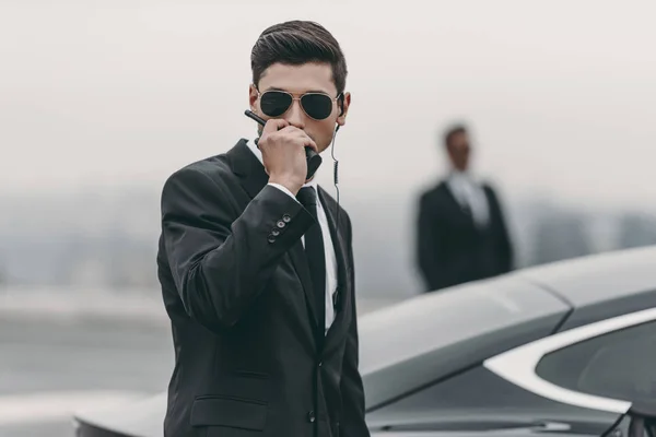 Guapo guardaespaldas en gafas de sol hablando por radio portátil - foto de stock