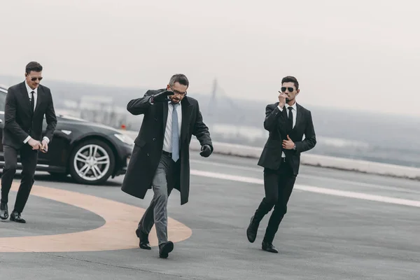 Businessman covering his face with hand and walking with bodyguards — Stock Photo