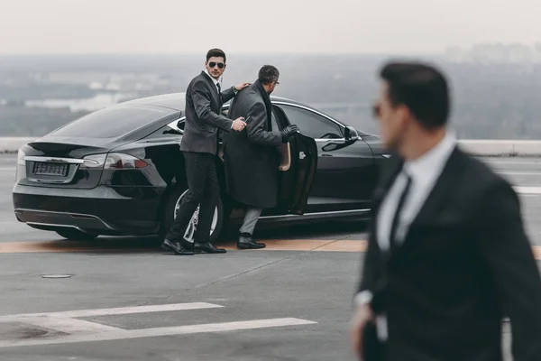 Bodyguard helping businessman to sit in black car — Stock Photo