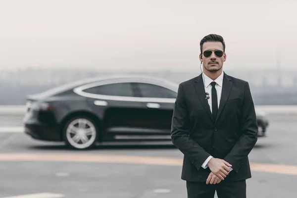 Serious bodyguard standing with sunglasses and security earpiece on helipad — Stock Photo