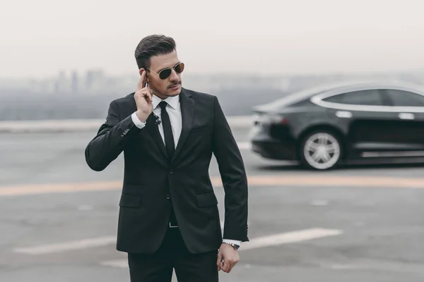 Serious bodyguard listening message with security earpiece on helipad — Stock Photo