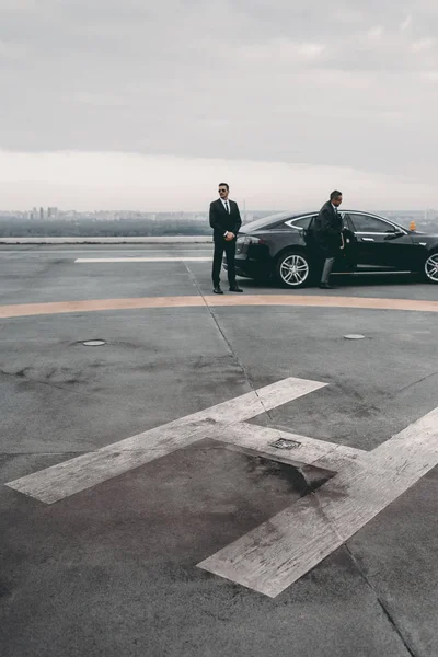 Bodyguard and businessman standing near car on helipad — Stock Photo