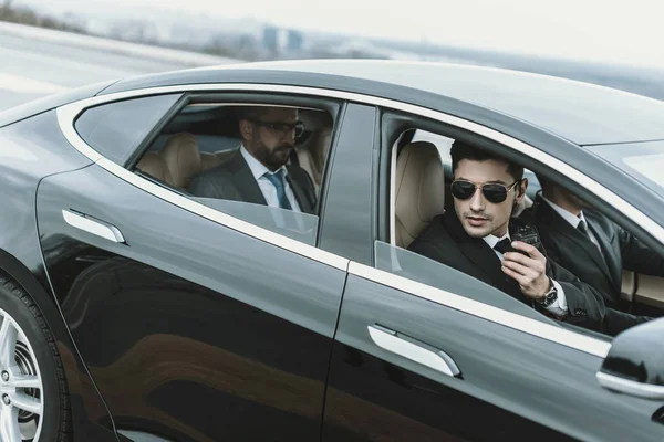 Bodyguards and businessman sitting in a black car — Stock Photo