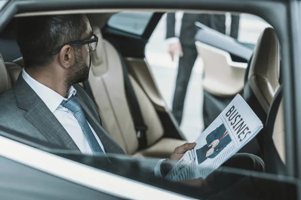 Businessman sitting in a car and holding newspaper — Stock Photo