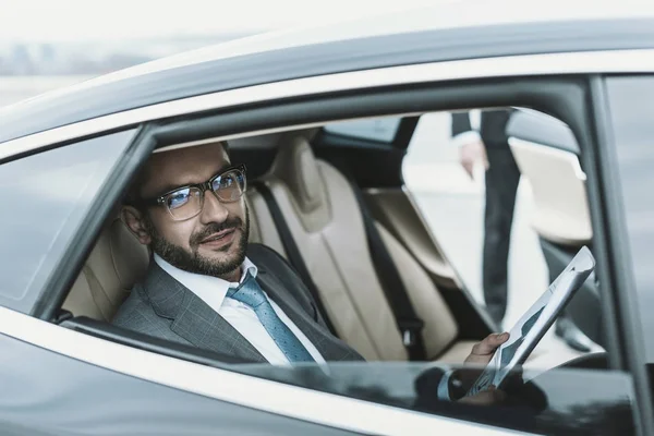 Hombre de negocios sentado en un coche con periódico y mirando hacia otro lado - foto de stock