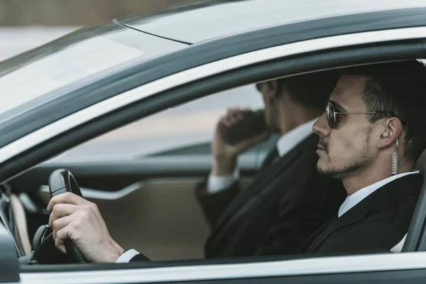 Guardaespaldas con radio portátil y auricular de seguridad sentado en un coche - foto de stock