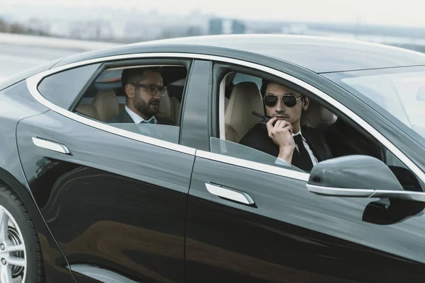 Guardaespaldas sentado en coche con hombre de negocios y hablando por radio portátil - foto de stock