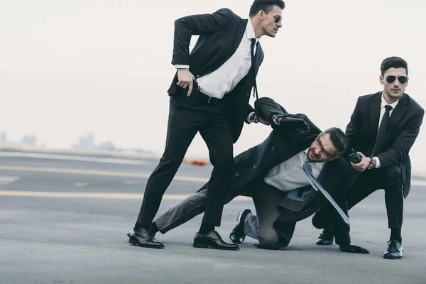 Dos guardaespaldas en gafas de sol protegiendo a hombre de negocios que cae - foto de stock