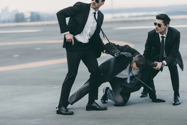 Imagen recortada de dos guardaespaldas protegiendo a hombre de negocios que cae - foto de stock