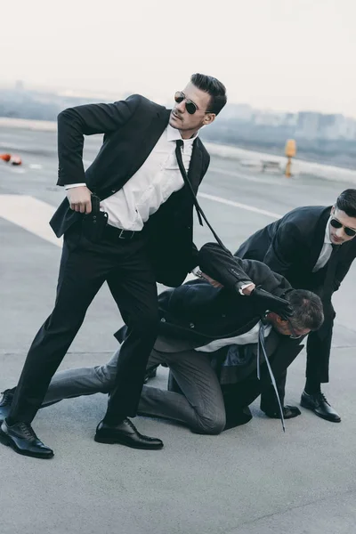 Dos guardaespaldas en gafas de sol protegiendo a hombre de negocios que cae - foto de stock