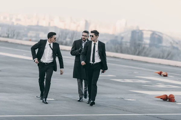 Businessman walking with bodyguards in sunglasses and suits on helipad — Stock Photo