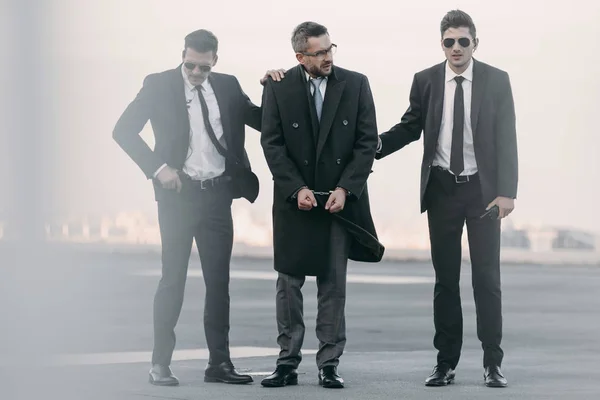 Security guards standing with arrested man on helipad — Stock Photo